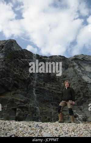 Geologie Student auf Charmouth, Dorset, fossile Jagd mit dem Jura blauen Lias Kalksteinfelsen und Wasserfall im Hintergrund. UK. Stockfoto