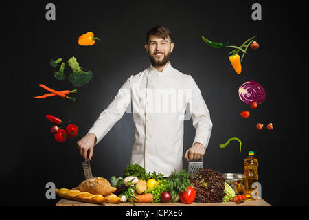 Mann Köchin hält eine Pfanne mit Gemüse in die Luft fliegen. Essen musikalischen Harmonie. Man kocht in der Küche. Menschen, Kochen, kulinarische und Food-Konzept. Ch Stockfoto