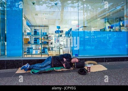 Mann schläft auf der Straße vor dem Schaufenster eines Schönheitssalons Stockfoto