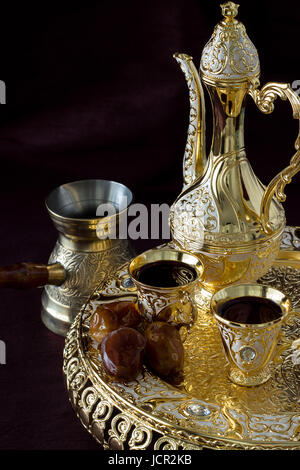 Stillleben mit traditionellen Goldenen arabischen Kaffee mit dallah, Kaffeekanne und Termine festgelegt. Der dunkle Hintergrund. Vertikale Foto. Stockfoto