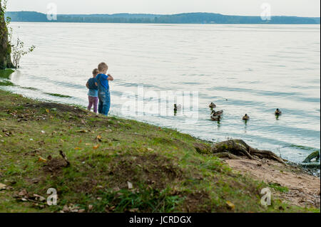 Zwei bezaubernde Schwestern füttern Enten an einem Fluss im Sommer Stockfoto