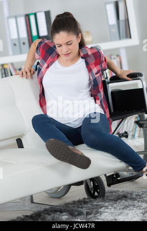 Rollstuhl-Benutzer versuchen, alleine auf dem Sofa sitzen Stockfoto