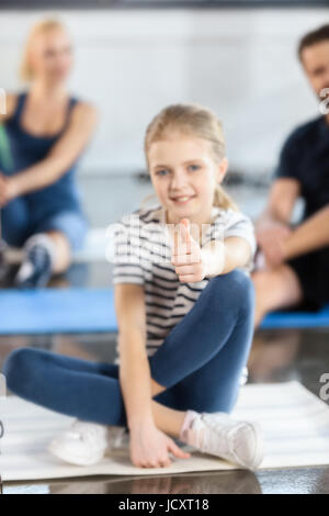 Süße blonde Mädchen sitzen auf Matte mit Daumen Stockfoto