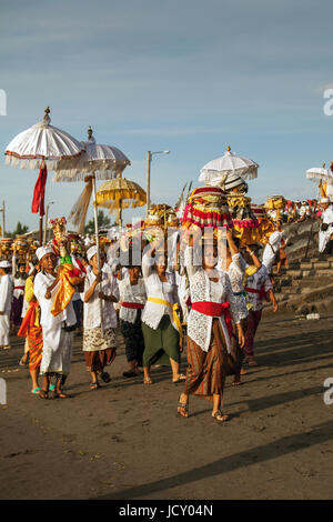 Melasti Ritual, jährliche Zeremonie der balinesischen Strand in Bali mit Gruppe von Menschen mit bunten Sonnenschirmen und religiöse Angebote auf ihren Köpfen am Strand Stockfoto