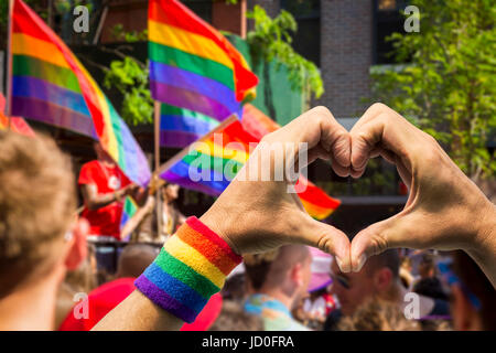 Unterstützende Hände machen Herzschild und winken vor ein Regenbogen Fahnen auf einem Schwimmer einer Sommer-gay-Pride-Parade Stockfoto