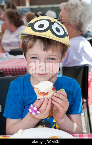 Ein kleiner Junge genießt das Essen einer Scone mit Marmelade und Sahne in eine Gemeinschaft Cream Tea Party in Wick Dorf, Chichester, England erstickt. Stockfoto