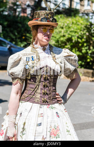 Steampunk Fashion. Frau, 20 Jahre, stehen mit Hand auf der Hüfte tragen Kleid mit Spitze vorne-up-Korsett und mit Brille und Feder. Im Freien, strahlendem Sonnenschein. Stockfoto