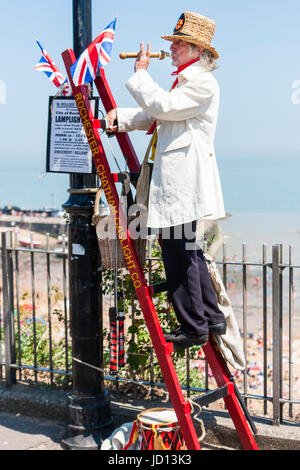 Herr William Thompkins, Anzünder, Charles Dickens Charakter, Geschichte. Das Tragen von weißen Mantel und Strohhut, steht auf Ladder gegen Licht mit Union Jack. Stockfoto