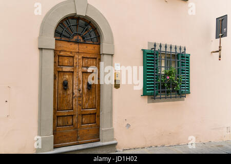 Gewölbte hölzerne Tür neben einem Fenster Wirh grüne Fensterläden, Bars und einen Blumenkasten. Stockfoto