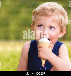 Süßes Kleinkind Baby junge achtzehn Monate alt, leckeres Eis über Hintergrund mit grünen Bokeh im Freien zu essen. Stockfoto