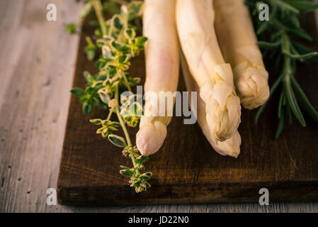 Horizontale Foto von mehreren Stücken weißen Spargel in dunklen Vintage Holzbrett mit grünen Kräutern wie Rosmarin und Thymian gebracht wird. Bo Stockfoto