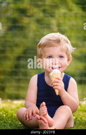 Süßes Kleinkind Baby junge achtzehn Monate alt, leckeres Eis über Hintergrund mit grünen Bokeh im Freien zu essen. Stockfoto
