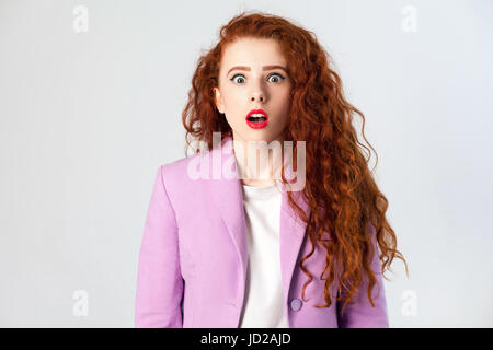 Porträt von schockiert schöne Geschäftsfrau mit rot - braune Haare und Make-up in rosa Anzug. Blick in die Kamera, drehte Studio auf grauem Hintergrund. Stockfoto