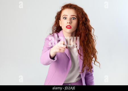 Porträt von schockiert schöne Geschäftsfrau mit rot - braune Haare und Make-up in rosa Anzug. zeigen und Blick in die Kamera, drehte Studio auf graue backgr Stockfoto