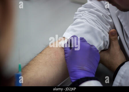 Arzt und Patient sitzt gegenüber von einander, während der Arzt eine Nadel herausziehen, das Blut des Patienten zu finden, bereitet Stockfoto