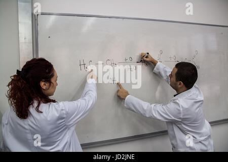 Junge Ärztinnen und Ärzte werden gedruckt, einige chemische Elemente auf eine weiße Tafel, versuchen, das Problem zu lösen Stockfoto