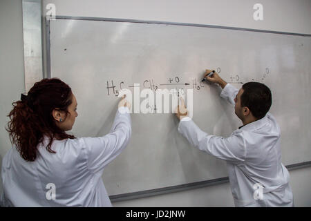 Junge Ärztinnen und Ärzte werden gedruckt, einige chemische Elemente auf eine weiße Tafel, versuchen, das Problem zu lösen Stockfoto