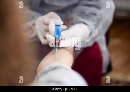 Arzt und Patient sitzt gegenüber von einander, während der Arzt eine Nadel herausziehen, das Blut des Patienten zu finden, bereitet Stockfoto