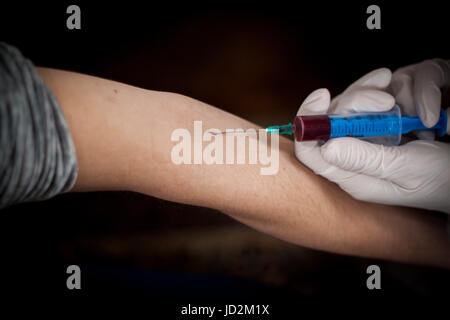 Arzt und Patient sitzt gegenüber von einander, während der Arzt eine Nadel herausziehen, das Blut des Patienten zu finden, bereitet Stockfoto