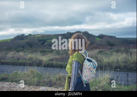 Eine junge Mutter ist Fuß in die Landschaft mit ihrem Baby im Tragetuch Stockfoto