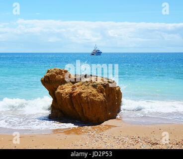 Wellen Waschen um einen Felsen am Praia Dona Ana und Yacht im Hintergrund, Algarve, Portugal Stockfoto