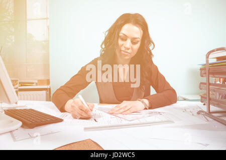 Frau an ihrem Schreibtisch mit Blaupausen vor Stockfoto