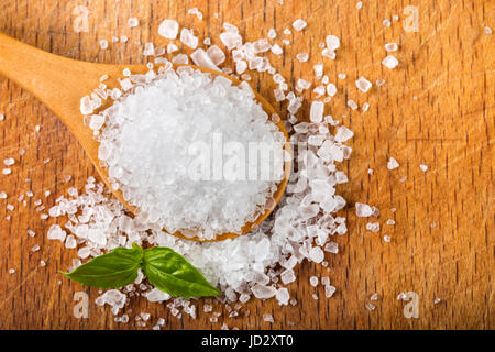 Meersalz in Holzlöffel mit Basilikum über Holz Hintergrund Stockfoto