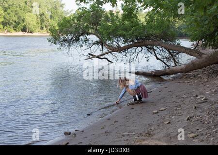 Eine junge Frau kauert nach unten und in das Wasser eines Flusses zu erreichen. Stockfoto