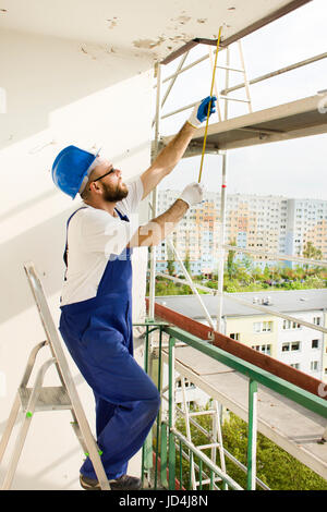 . Bauarbeiter in einem Schutzhelm und Arbeit Kleidung Maßnahmen Gerüst auf einer Baustelle Stockfoto