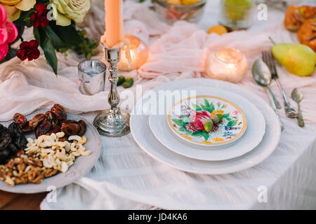 Hochzeit, Dekoration, Einstellung, Vegetarismus, Lifestyle-Konzept - Stillleben von Table linens mit schneeweißen drapieren, Platten mit Blumendruck, Kerzen, Tafelsilber, Haufen von Blumen und Nüssen Stockfoto