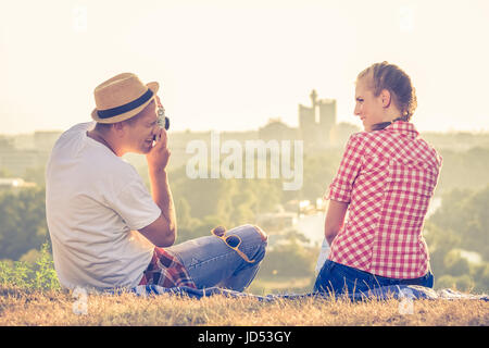 Trendige jungen Mann mit Hut nehmen Foto von seiner Freundin auf Hügel oberhalb der Stadt mit Retro-Kamera. Liebe, Sommer und Reisen Konzepte. Stockfoto