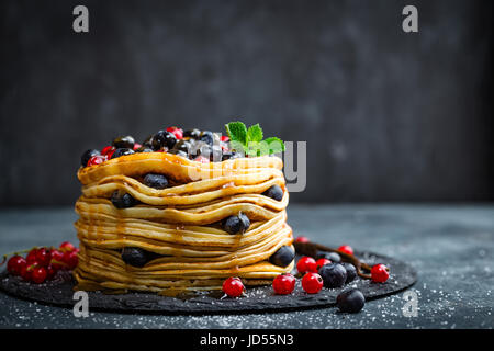 Pfannkuchen mit frischen Beeren und Ahornsirup auf dunklem Hintergrund, Nahaufnahme Stockfoto