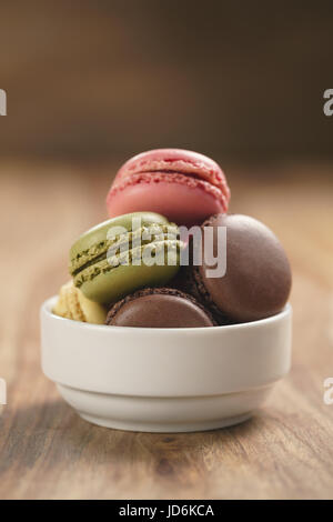 sortierte Macarons in weiße Schüssel auf Holztisch Stockfoto