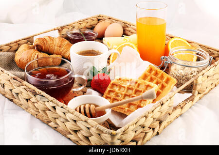 Frühstück im Bett mit Obst und Gebäck auf einem Tablett-Waffeln, Croissants, Kaffee und Saft Stockfoto