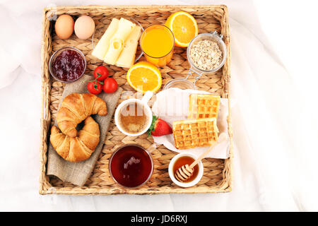 Frühstück im Bett mit Obst und Gebäck auf einem Tablett-Waffeln, Croissants, Kaffee und Saft Stockfoto