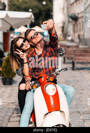 Junges attraktives paar Teenager trägt Sonnenbrille auf Retro-Motorrad macht Selfie, sonnige Straße, urban Hipster-Konzept Stockfoto