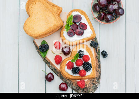 Schüssel gefüllt mit Kirschen und herzförmige Kekse mit Quark, Kirschen und einem Zweig Minze präsentiert auf einem Baum Datenträger verteilt Stockfoto