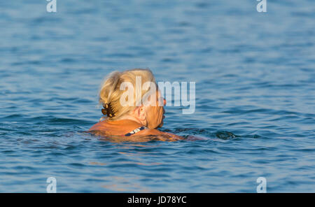 Ältere Dame, die am frühen Morgen schwimmen im Meer an einem warmen Sommermorgen in Großbritannien. Stockfoto