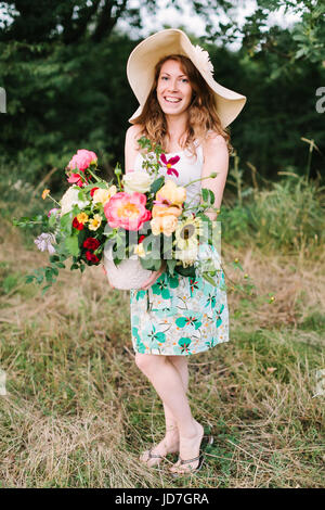 Bouquet, Menschen, Blumen Urlaub, Geschenk und Blumenarrangement Konzept - schöne weibliche Blumenladen in einem modischen Hut posiert mit Bouquet von frischen Blumen auf Grund der Bäume, lächelnde Frau. Stockfoto