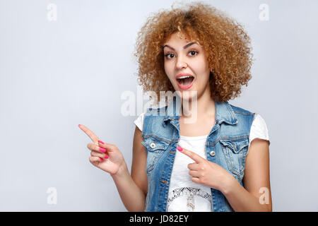 Porträt von lustigen schönen lockigen Mischlinge Mädchen im casual-Stil zeigt. Blick in die Kamera. Studio auf hellgrauen Hintergrund gedreht. Stockfoto