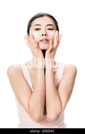 Junge Frau, die sanfte Anti-Aging Feuchtigkeitscreme auf ihren Wangen vor weißem Hintergrund anwenden Stockfoto