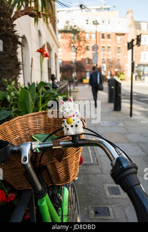 Maneki Neko (japanische verlockende Katze) auf einem Fahrrad in Fitzrovia, London, UK Stockfoto