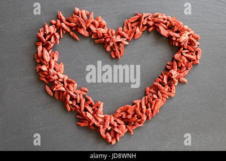 Die Form eines Herzens, hergestellt aus getrockneten Goji-Beeren auf einem dunklen Hintergrund Stockfoto