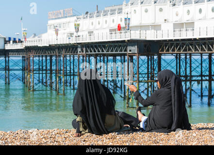 Junge Frauen trägt einen schwarzen Tschador, während er auf dem Kiesstrand an einem heißen sonnigen Tag in Brighton, East Sussex, England, UK. Stockfoto