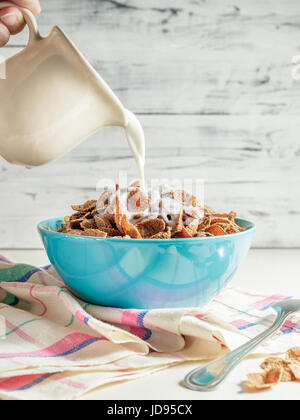 Gießen die Milch in die Schüssel mit Weizen Buchweizen Kleie Getreide. Gesundes Frühstück-Konzept Stockfoto