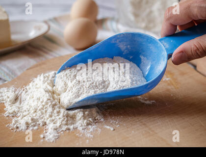 Weizenmehl in blauen Plastiklöffel auf Holzbrett mit Backzutaten auf dem Hintergrund Stockfoto