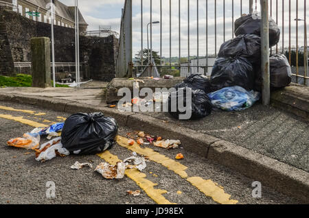 Ein split schwarz Müllbeutel mit teilweise verschüttet Inhalt von Hausmüll ist in der Nähe von anderen Taschen am Straßenrand aufgetürmt. Stockfoto