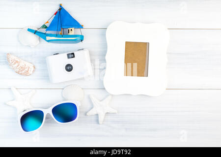 Strand-Accessoires (weiße Sonnenbrille, Seestern, Kamera, Boot, Shell) und weiße Vintage Bilderrahmen auf weißem Gips Holz Tischplatte Ansicht, Sommer Urlaub con Stockfoto