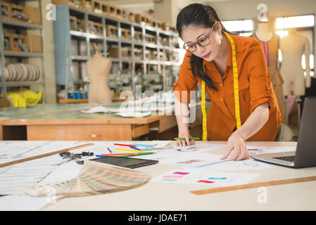 schöne Mode Designer Entscheidung Frau auf der Suche nach besten Markt-Design-Skizze mit Stoffmuster in der Herstellung von Büro Studio übereinstimmen. Beruf und Stockfoto