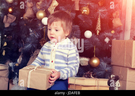 Kleiner Junge hält Weihnachtsgeschenk in der Nähe von Tanne Stockfoto